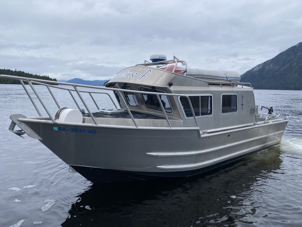 A sturdy, custom-built Alaska Ocean Safaris fishing boat floating on calm waters with scenic mountains in the background in Ketchikan, Alaska.